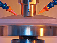 Close-up of a laboratory testing machine with a probe and coolant nozzles above a cylindrical sample