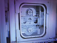 Semiconductor manufacturing machine with circular wafers visible through a glass window.