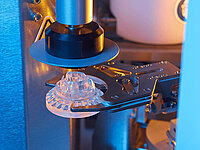 Close-up of a machine arm holding and processing an optical lens.