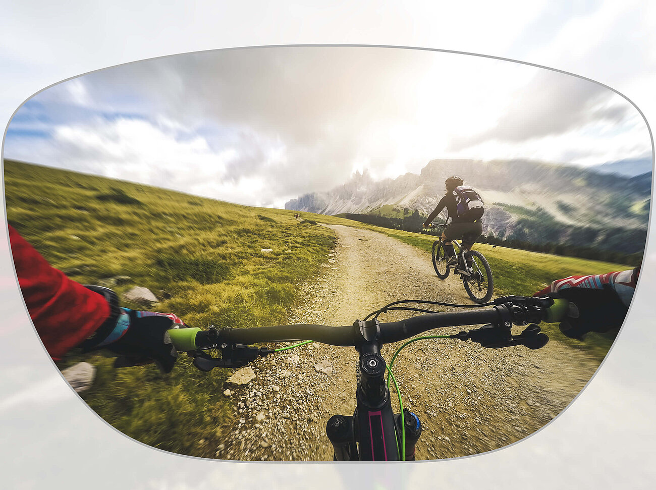 View through a pair of glasses showing two cyclists riding on a mountain trail with a scenic landscape in the background.