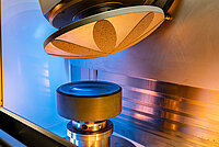 Close-up of laboratory equipment with a conical tool positioned above a cylindrical sample