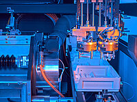 Automated production machine with robotic arms placing glass lenses into transport boxes.