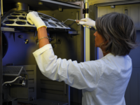 Technician wearing gloves loading semiconductor wafers into a holder inside processing equipment.
