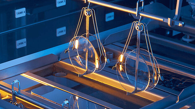 Semiconductor wafers suspended by metal holders above a processing bath in a cleanroom environment.