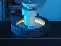 Close-up of a precision machine tool working inside a circular holder, illuminated with blue light.