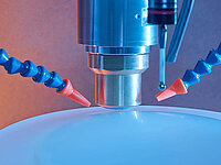 Close-up of laboratory equipment with a probe and coolant nozzles above a rounded sample surface