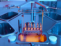Multiple semiconductor wafers held in a rack being lowered into a chemical bath within a processing station.