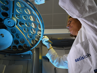 Technician in a Satisloh lab coat working with an optical lens holder inside a coating machine.