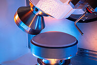 Close-up of a laboratory machine with a conical tool positioned above a cylindrical sample