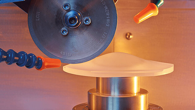 Close-up of a Satisloh precision optics grinding machine processing a lens.