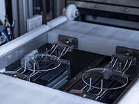 Two circular glass wafers held in metal clamps inside a semiconductor manufacturing machine.