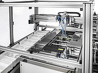 Automated production machine with robotic arms and conveyor system for handling components.