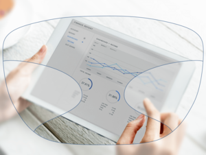 View through a pair of glasses showing hands holding a tablet with charts and graphs on the screen.
