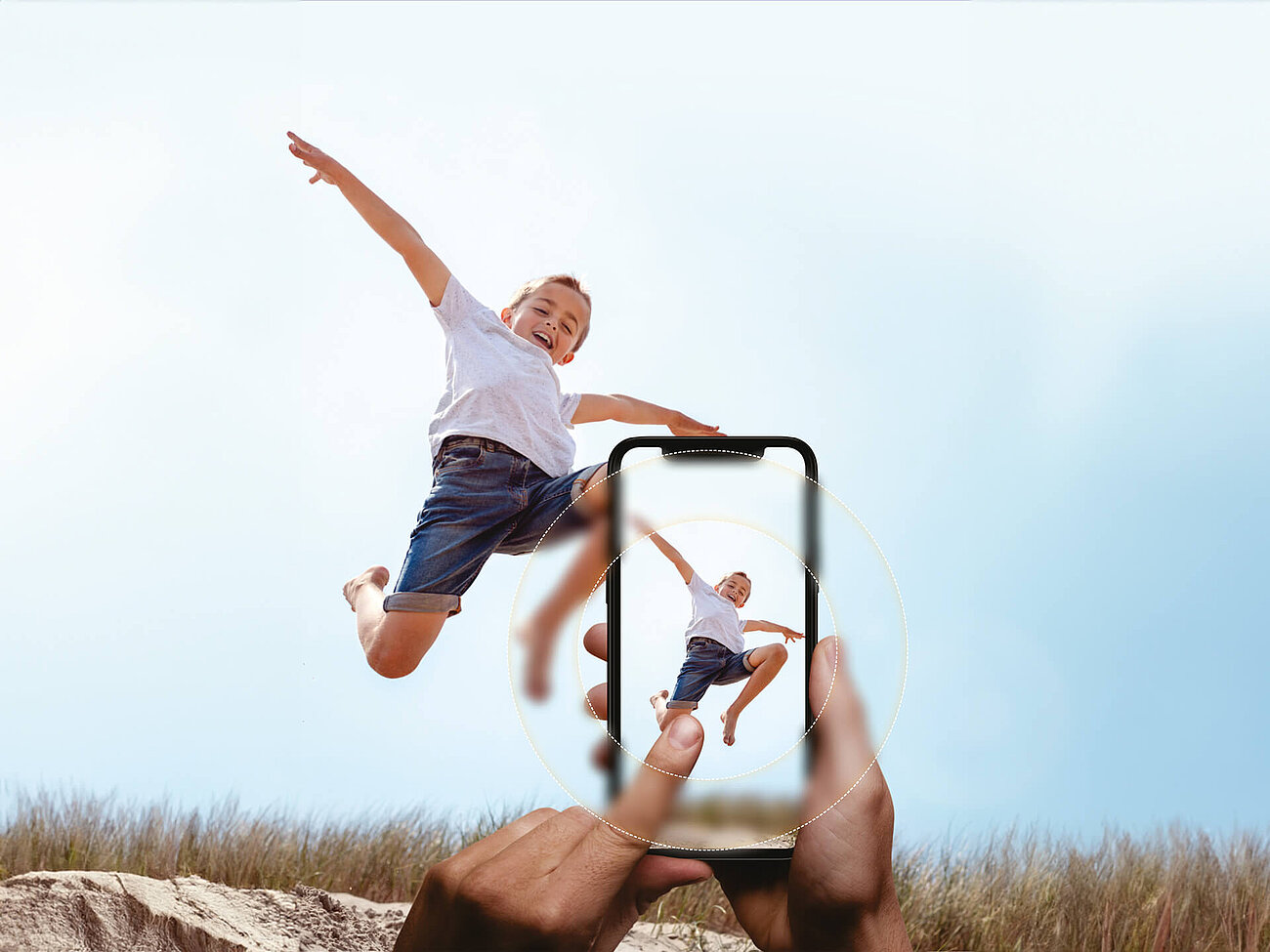 Child jumping joyfully in the air while being photographed with a smartphone in the foreground.