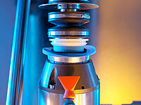 Close-up of an industrial machine holding and processing a glass lens with precision tools.