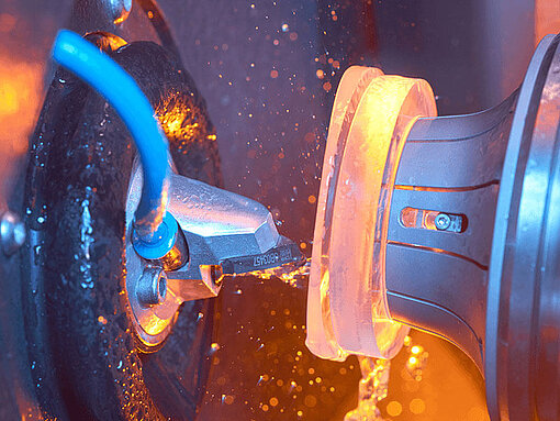 Close-up of a glass lens being processed in a machine with coolant and spark formation.