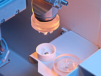 Industrial machine precisely positioning or processing a glass lens in a holder.