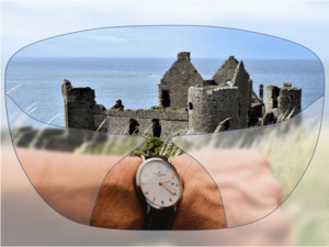 View through a pair of glasses showing ruins of a stone castle by the sea, with a wristwatch visible in the foreground.