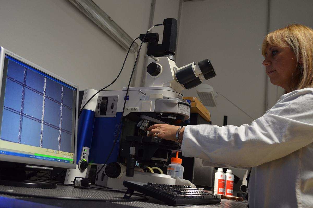 Scientist using a microscope connected to a computer screen displaying analysis results.