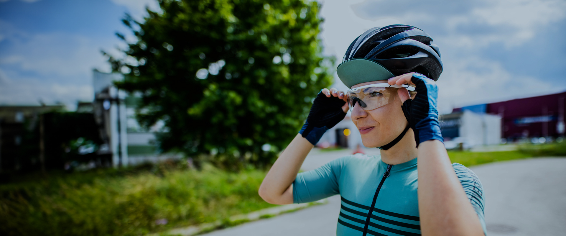 Unleash your potential Cyclist wearing a helmet and sportswear, adjusting their glasses outdoors on a sunny day.