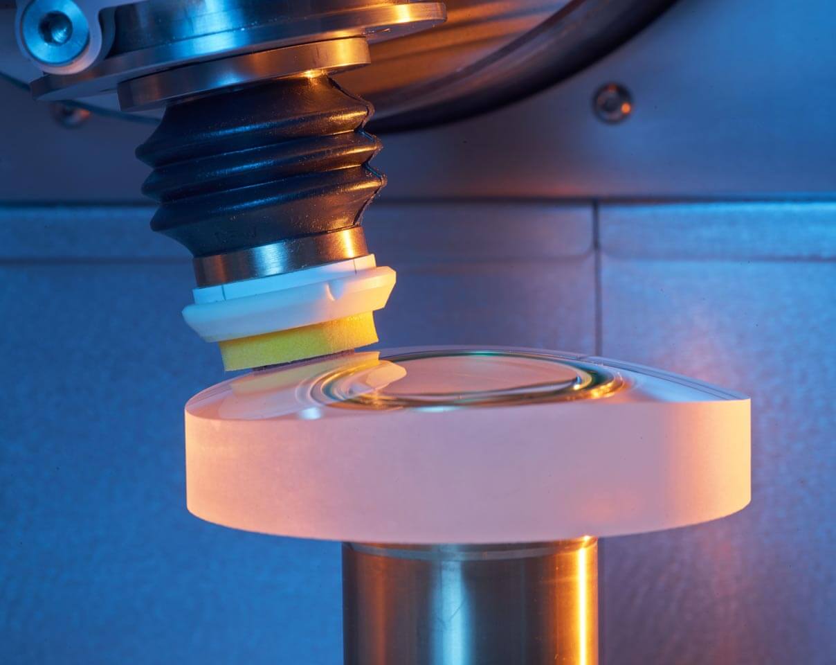Close-up of a Satisloh machine polishing a lens during the precision optics manufacturing process.